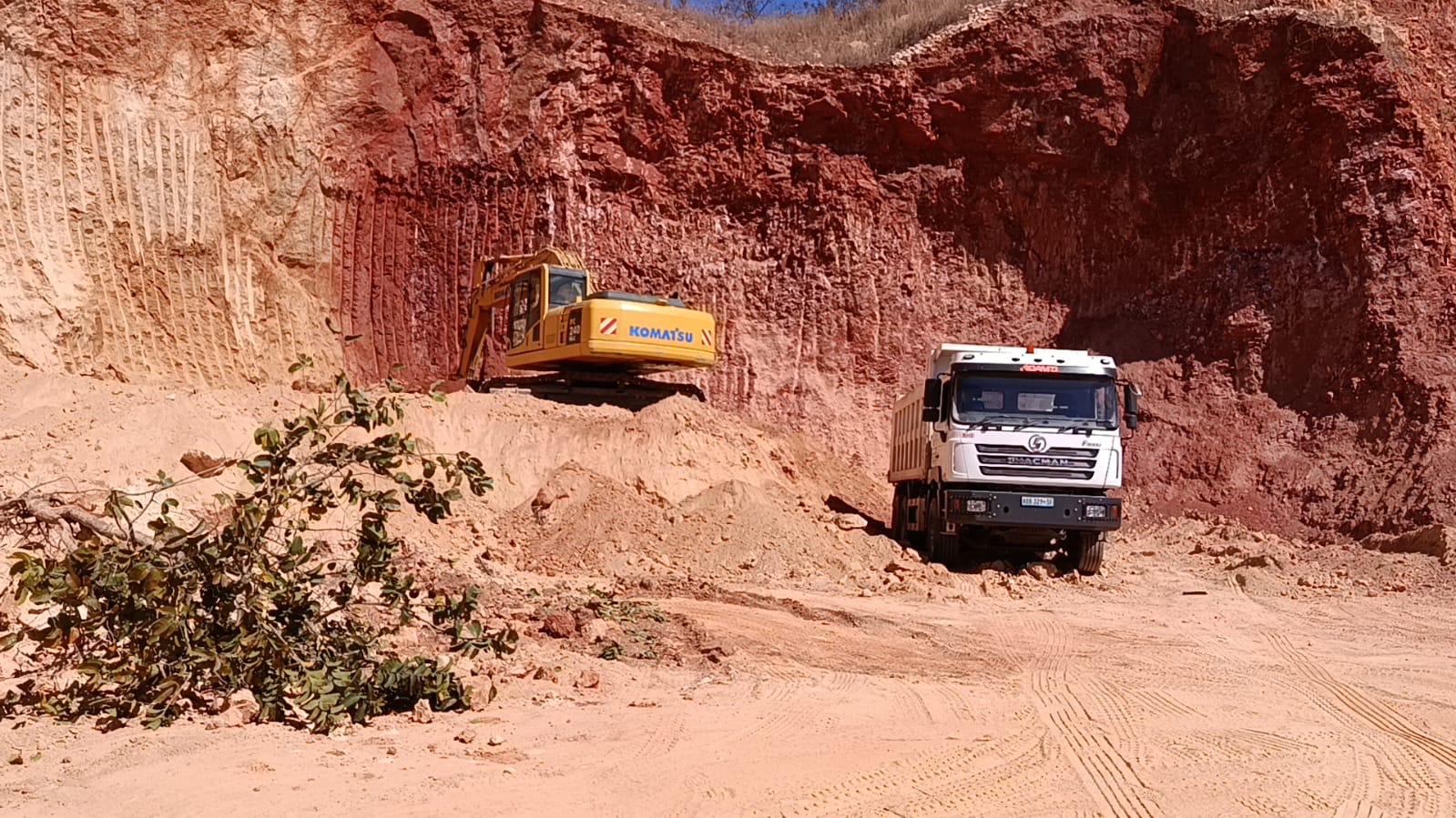 Escavadora Komatsu e basculante Shacman branco em frente de extracção de solos
