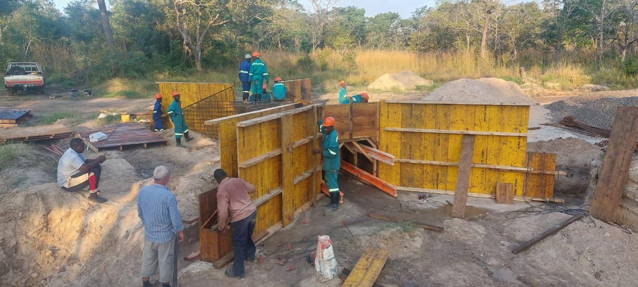 Trabalhadores com equipamento de protecção a montar cofragem amarela numa vala