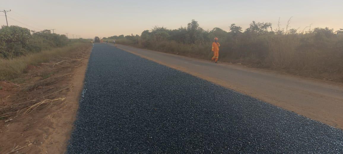 Faixa de estrada com camada asfáltica nova e trabalhador de fardamento laranja