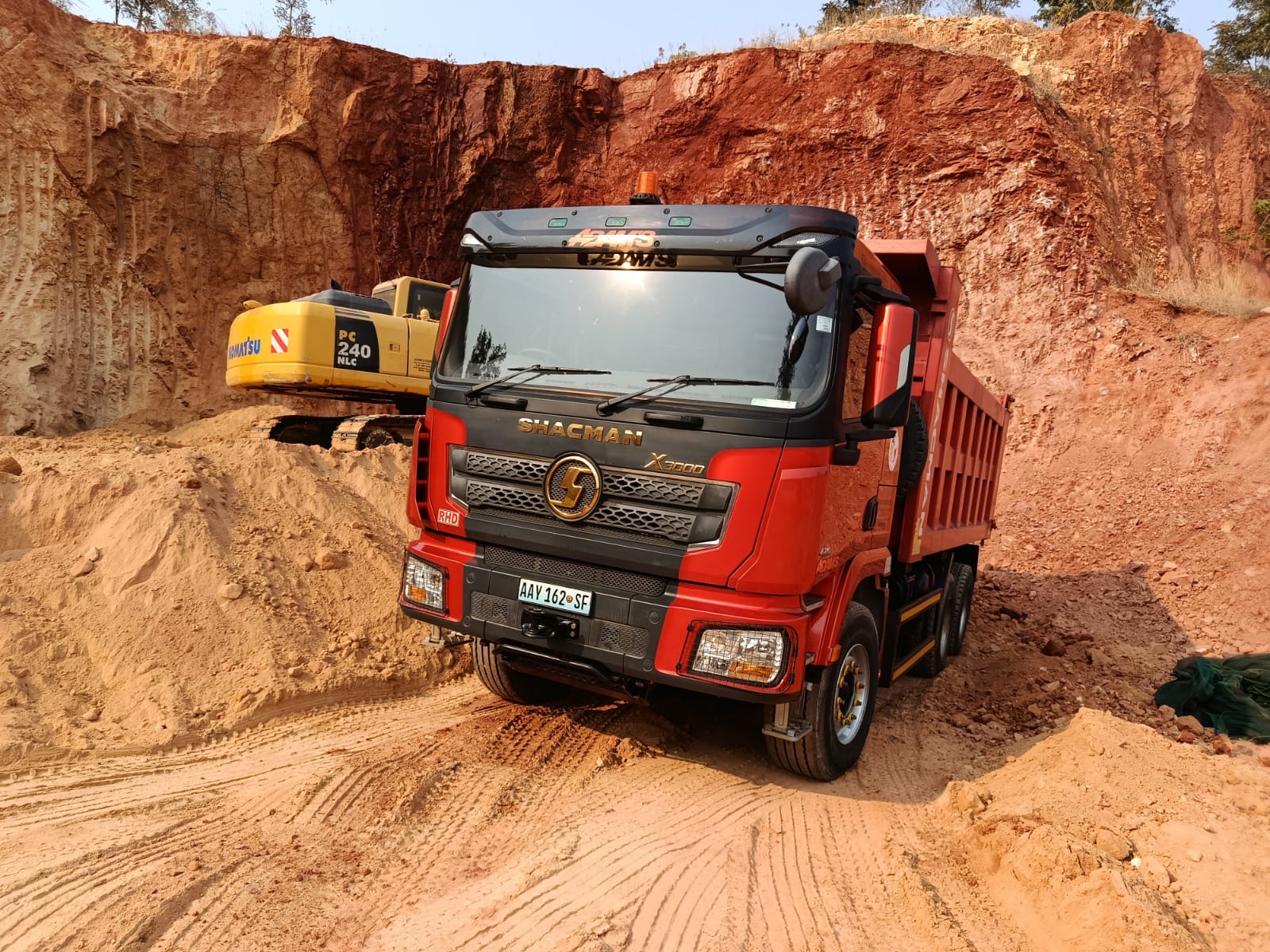 Basculante Shacman X3000 vermelho da Adam's em pedreira com escavadora Komatsu